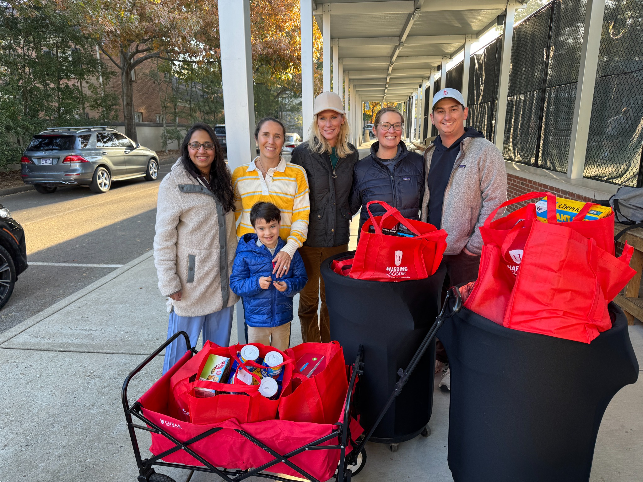 Harding volunteers and a child standing beside red bags filled with donated food