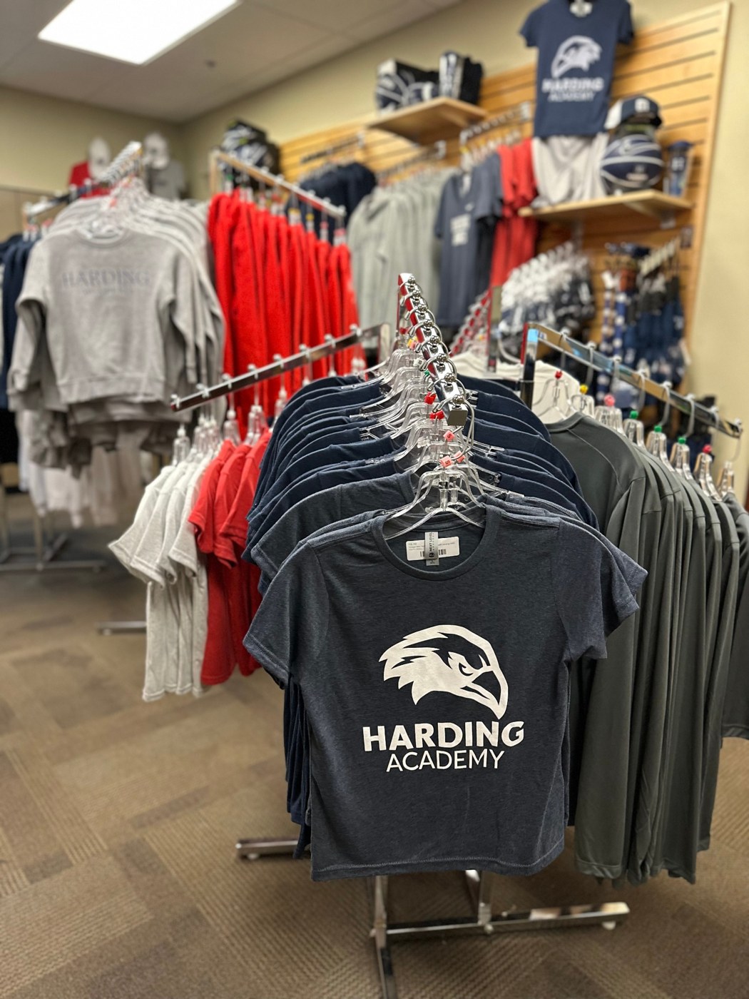 Navy, red, and gray Harding shirts on clothing racks inside the School Store